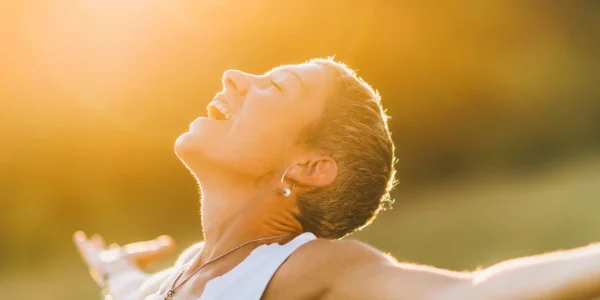 Ein Moment der Offenheit, eingefangen in einem Bild: Eine Person steht in der goldenen Stunde des Sonnenuntergangs, Arme weit geöffnet, das Gesicht zur Sonne erhoben, in einem Ausdruck purer Freude und Befreiung. Die Wärme des Lichts umhüllt die Szene, unterstreicht das Gefühl der Verbundenheit mit der Natur und der Welt. Ein Sinnbild für die Offenheit gegenüber den Geschenken des Lebens.