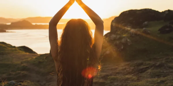 Eine Person meditiert in der Abendsonne auf einem Hügel. Die Silhouette gegen den warmen Himmel vermittelt Harmonie und erzeugt eine Atmosphäre von Frieden und Spiritualität.