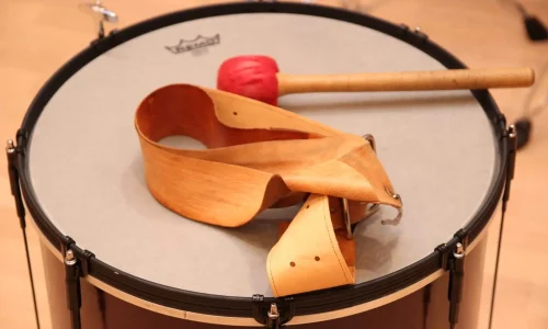 Auf dem Bild ist eine Trommel aus nächster Nähe zu sehen, die für die TaKeTiNa®-Rhythmustherapie verwendet wird. Ein roter Schlägel liegt bereit auf der Oberfläche der Trommel, daneben befindet sich ein traditioneller Holzgürtel, der typisch für diese einzigartige musiktherapeutische Methode ist. Die TaKeTiNa®-Methode nutzt Rhythmus und Musik als Mittel zur Förderung von Entspannung, Präsenz und innerer Harmonie. Diese Szene fängt die Essenz von TaKeTiNa® ein: die Verbindung von Rhythmus, Bewegung und Klang, um einen tiefen Zustand der Achtsamkeit und Selbstfindung zu erreichen.