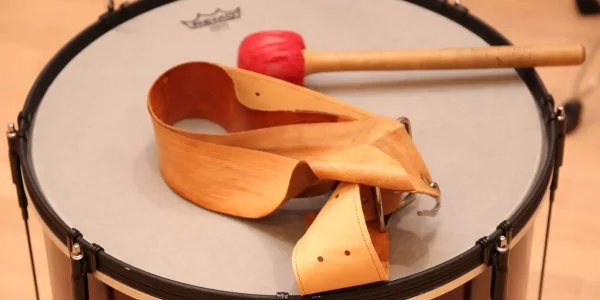 Auf dem Bild ist eine Trommel aus nächster Nähe zu sehen, die für die TaKeTiNa®-Rhythmustherapie verwendet wird. Ein roter Schlägel liegt bereit auf der Oberfläche der Trommel, daneben befindet sich ein traditioneller Holzgürtel, der typisch für diese einzigartige musiktherapeutische Methode ist. Die TaKeTiNa®-Methode nutzt Rhythmus und Musik als Mittel zur Förderung von Entspannung, Präsenz und innerer Harmonie. Diese Szene fängt die Essenz von TaKeTiNa® ein: die Verbindung von Rhythmus, Bewegung und Klang, um einen tiefen Zustand der Achtsamkeit und Selbstfindung zu erreichen.